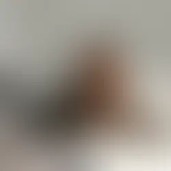 Woman with glasses reading a book on a bed, staying up at night due to pitta and insomnia. surrounded by gray pillows and blankets.