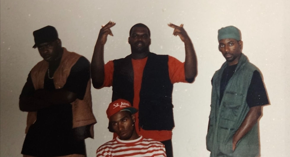 Four men posing; one points fingers up