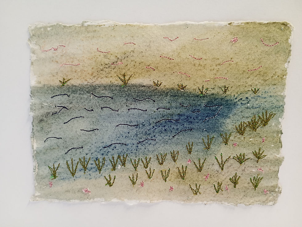 An embroidered textile artwork of water and surrounding grasses with leaves and flowers stitched on to paper.