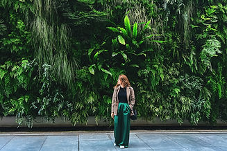 Stylish dressed woman standing near the lush green wall in urban garden.jpg