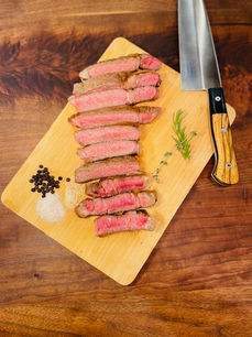 Sliced medium rare steak on a cutting board with herbs, salt, and pepper from Weller Beef.