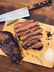 Sliced medium rare steak on a cutting board with herbs, salt, and pepper from Weller Beef.