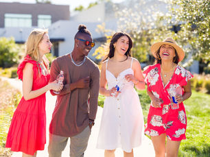 a group of 4, 3 females and 1 male, laughing outdoors drinking smart water.