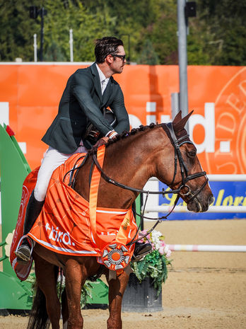 Chris Fellers pets Dawsons Gold after winning a grand prix at Thunderbird Show Park. Dawsons Gold wears a bright orange cooler and a large orange first-place ribbon.