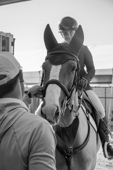 Equestrian coach, Chris Fellers, adjusts student's bridle as they debrief after a clear round at DIHP