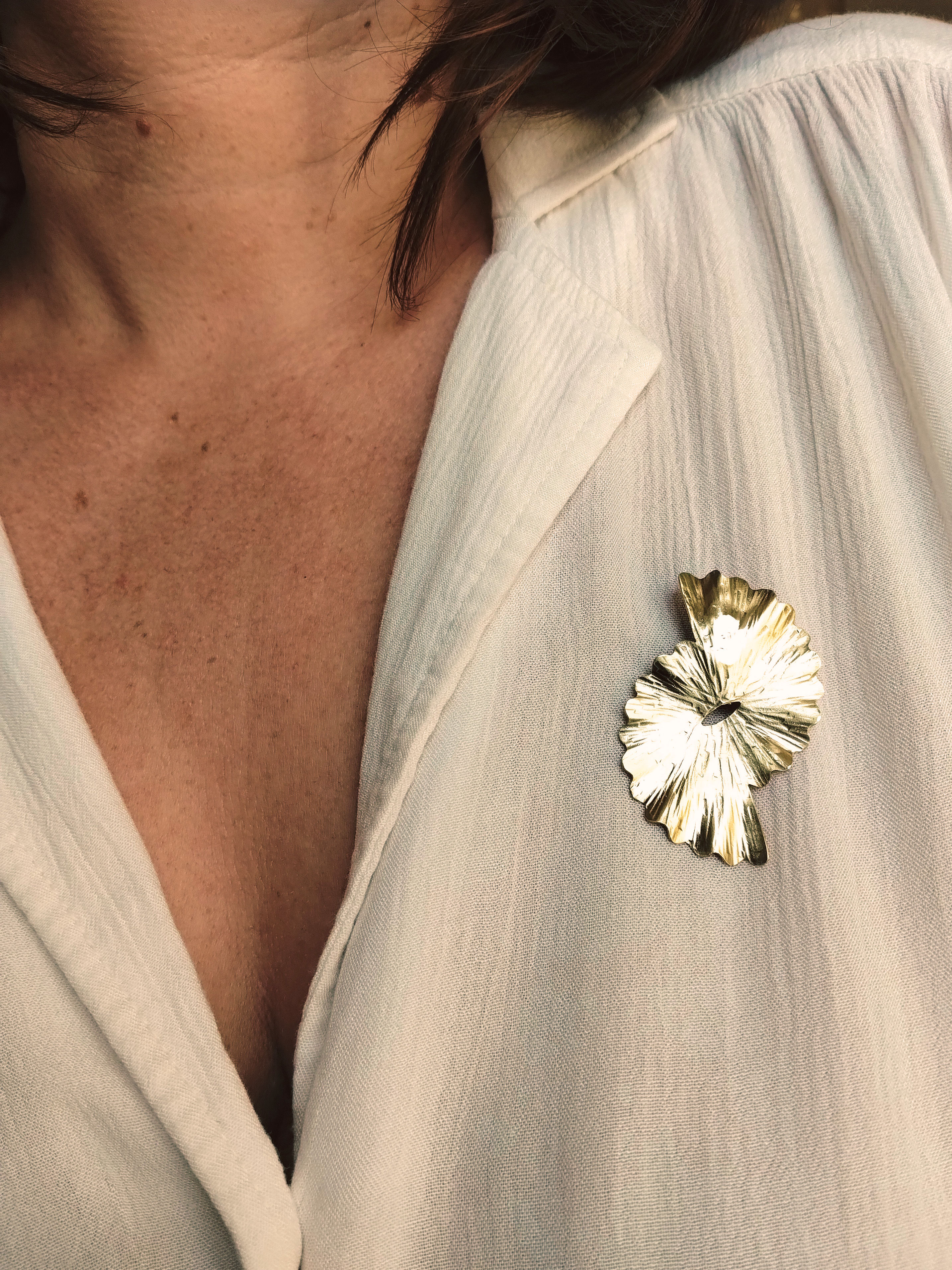 Broche dorée surmontée d'une forme dentelée et martelée en rayons.