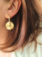Boucles d'oreilles créoles dorées composées d'un anneau ovale et de d'un pendentif ondulé et dentelé en forme de fleur.