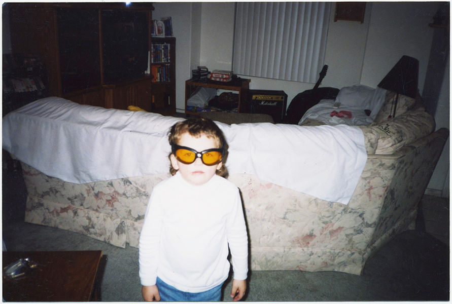 BOY with FRWAKY ORANGE GOGGLES in DOMESTIC INTERIOR!  Weird!