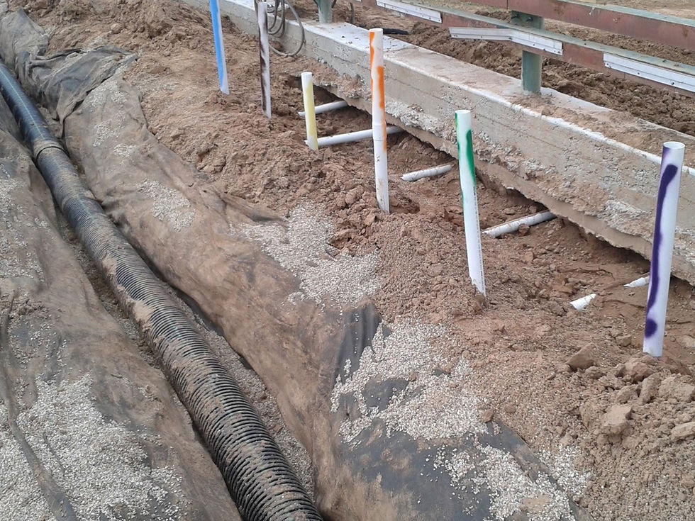Color-coded irrigation stakes and drainage pipe installed during construction on a bond-funded sports field project in Texas.