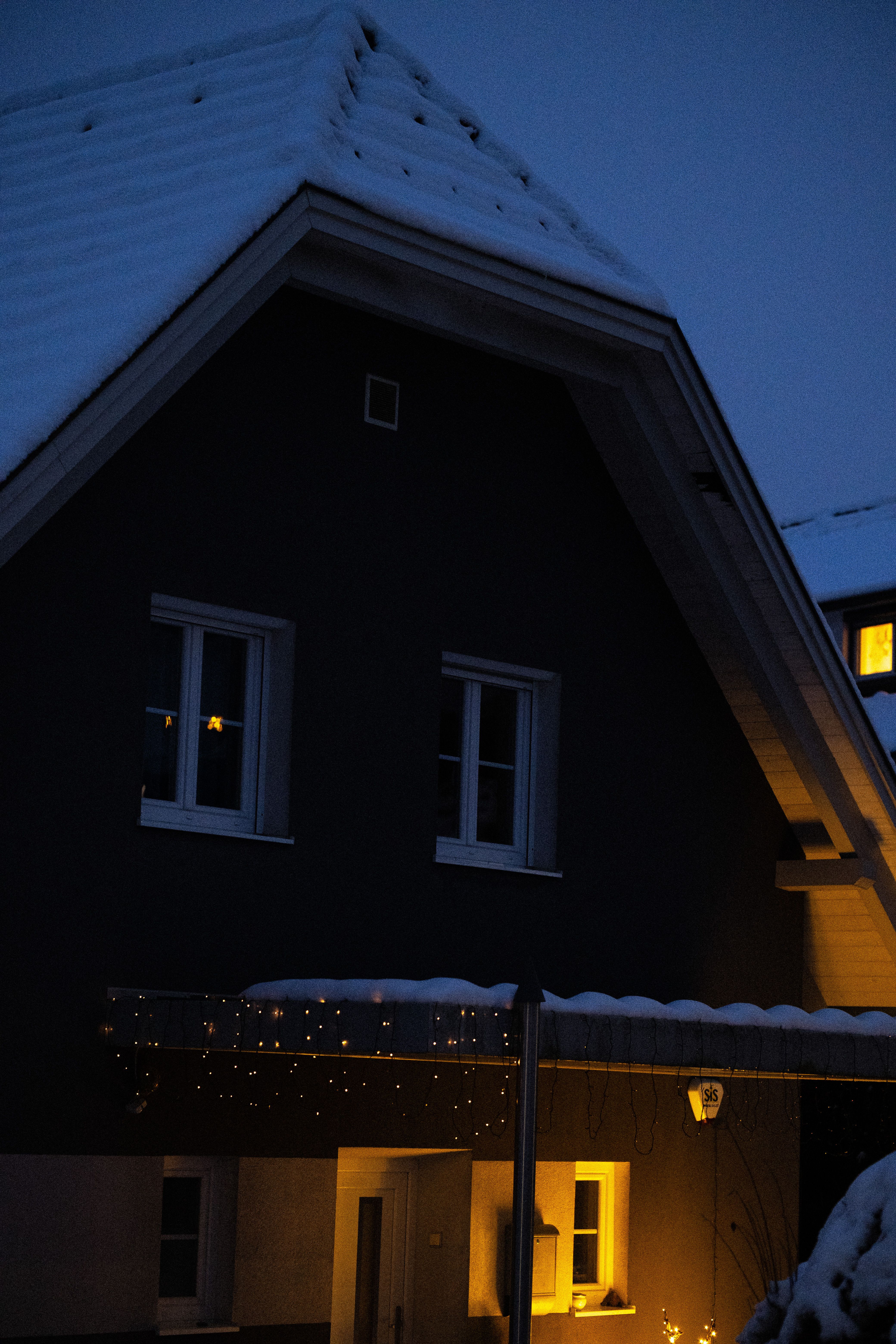A house at dusk in deep snow, warm gold light spilling from its windows and entry.