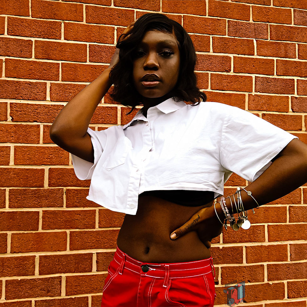 Woman in white crop top, red pants, against brick wall.
