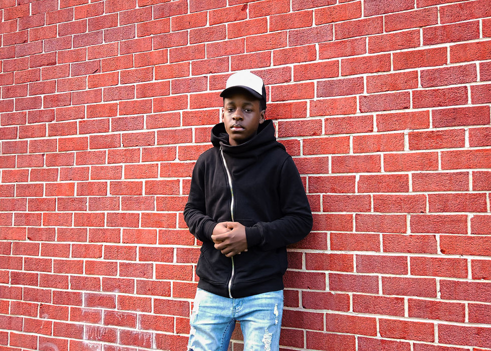 Young boy in black hoodie and white cap against brick wall