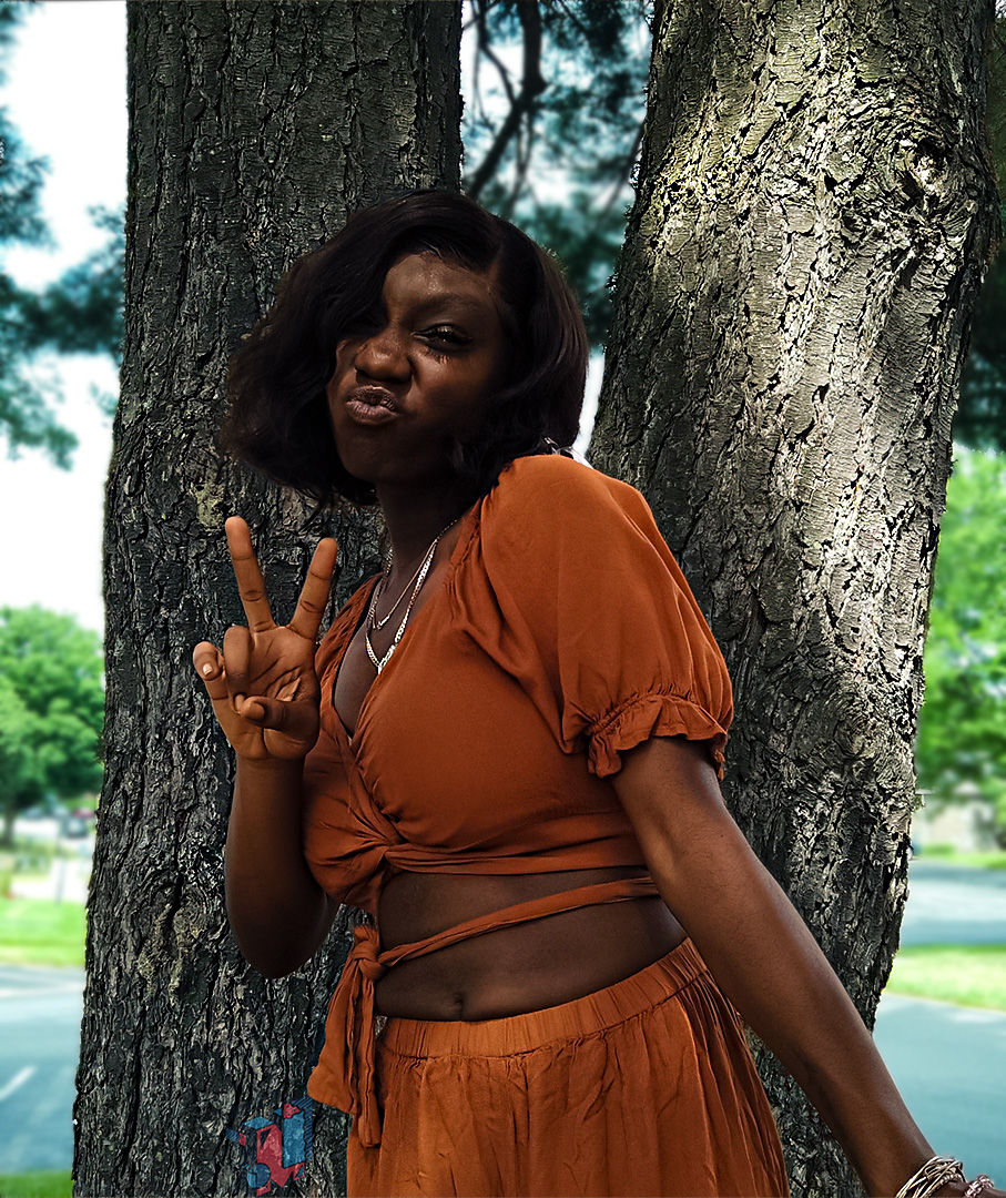 Woman pouting with peace sign by tree