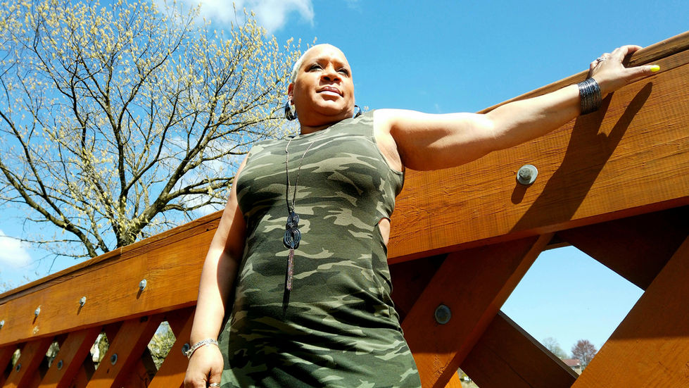 Woman in camo dress leaning on a wooden railing outdoors
