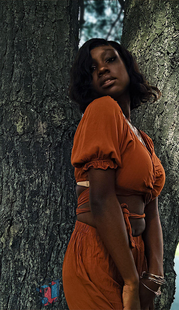 Woman in orange outfit posing by a tree