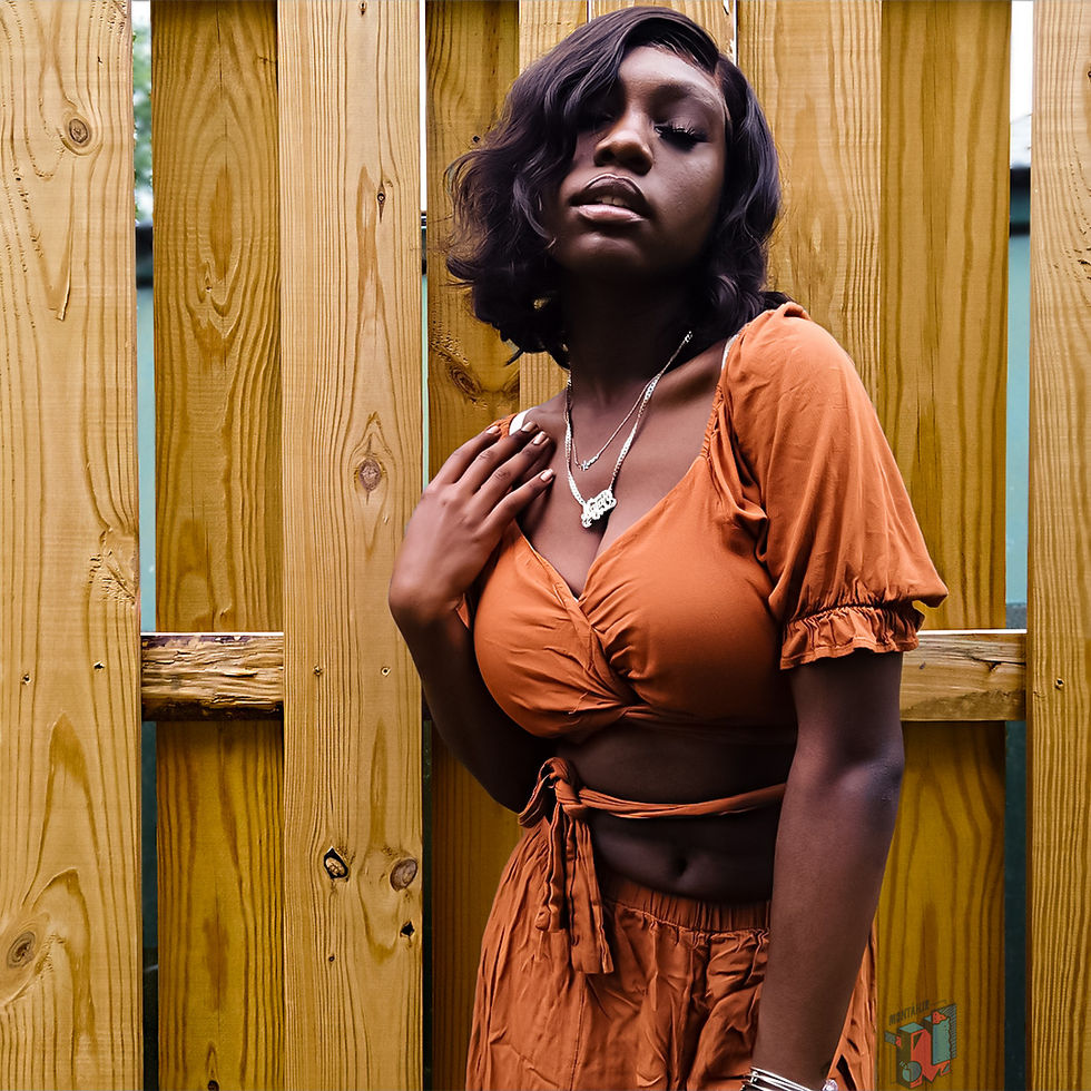 Young woman in orange outfit posing by wooden fence