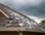 Hail accumulation on the roof highlights the aftermath of a recent storm under dark, looming clouds.