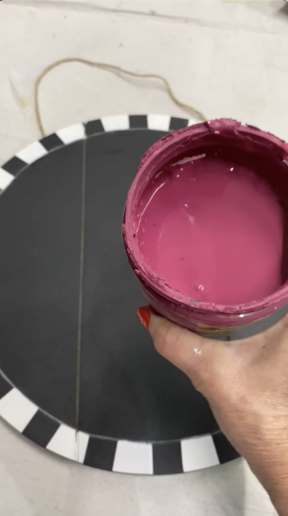 Tracey's Fancy holding a container of plum crazy that she is about to use to paint the background of her DIY door hanger