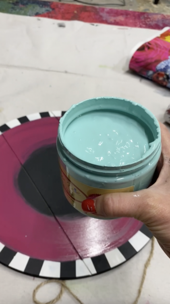 Tracey's Fancy holding up a jar of the Gulf chalk mineral paint that she is about to use to create a blended background for her DIY door hanger