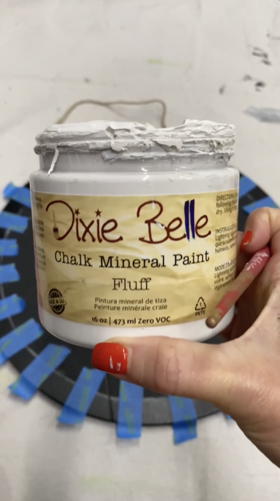 Tracey's Fancy holding up a container of Dixie Belle chalk mineral paint in fluff as she's about to apply it on her DIY door hanger