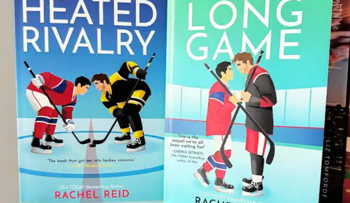 Two professional hockey players in uniform face each other closely, almost forehead to forehead, with intense expressions. The background is a blurred ice rink, and the title Heated Rivalry appears in bold red letters, emphasizing tension and passion.