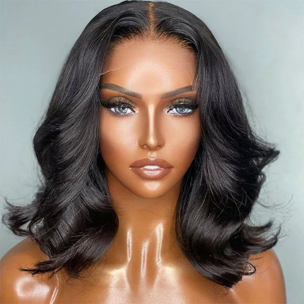 A person with wavy black hair and striking makeup poses against a plain background, exuding a confident and polished look.