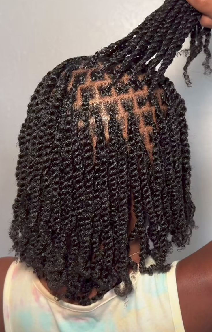 Close-up of a person with neatly parted and twisted black hair held up, showcasing the pattern. They wear a tie-dye tank top.