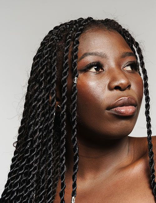 A dark skin woman with senegalese twist hair style, set against a plain white background. Her expression is empowering and confident.
