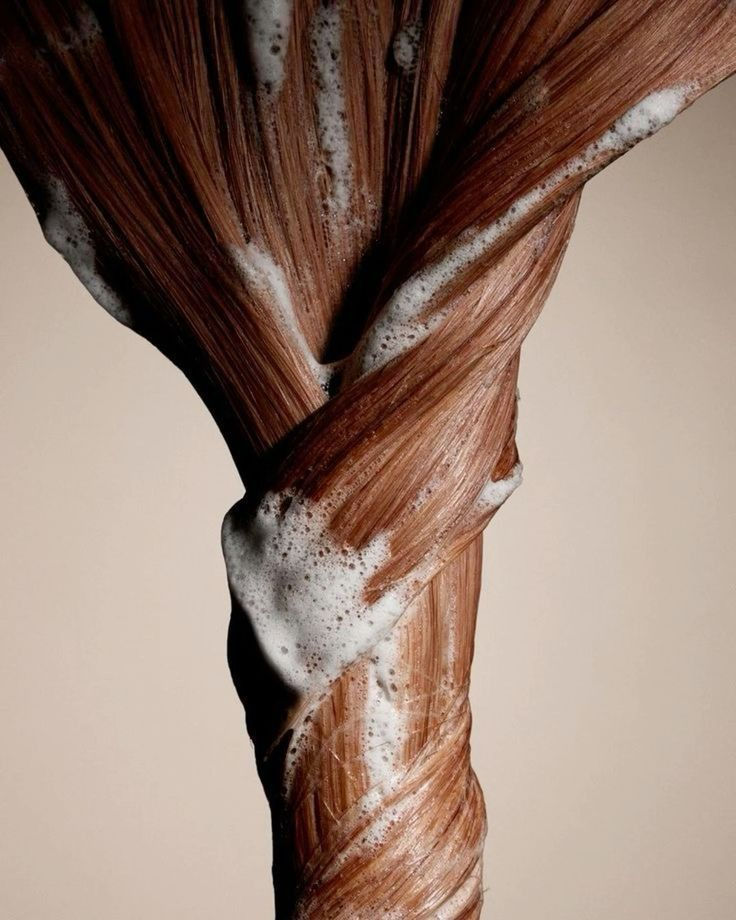 Close-up of brown hair tightly coiled with white foam, set against a beige background. The texture is sleek with a glossy finish.
