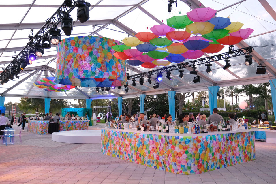 Clear top tent with large lamp and umbrella ceiling installations for welcome party event.