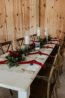 Wedding reception table with greenery, burgundy flowers, and glass enclosed candles at The Evermore in Apex, NC