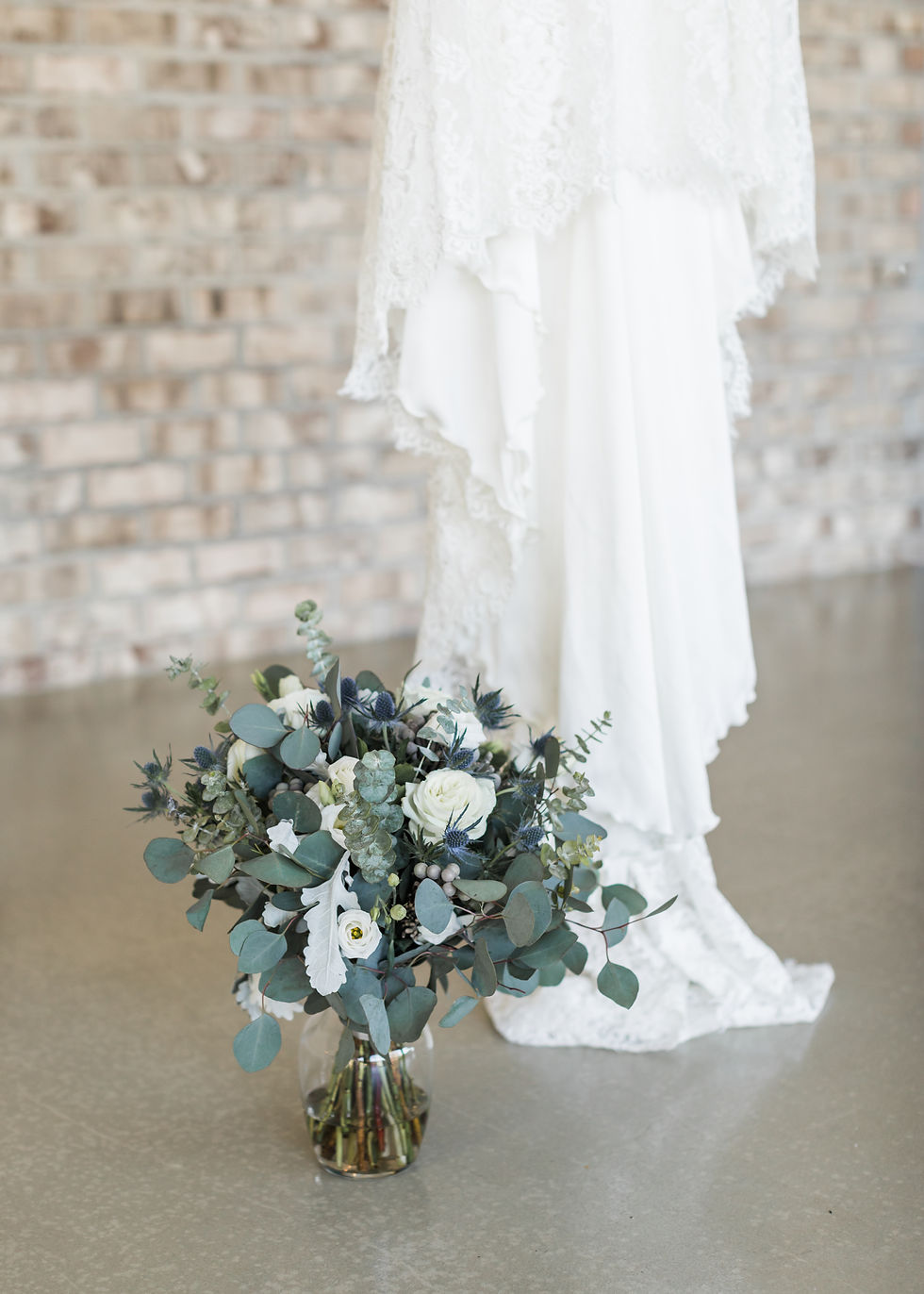 Romantic white and blue bridal bouquet with eucalyptus and thistle beside a lace wedding dress