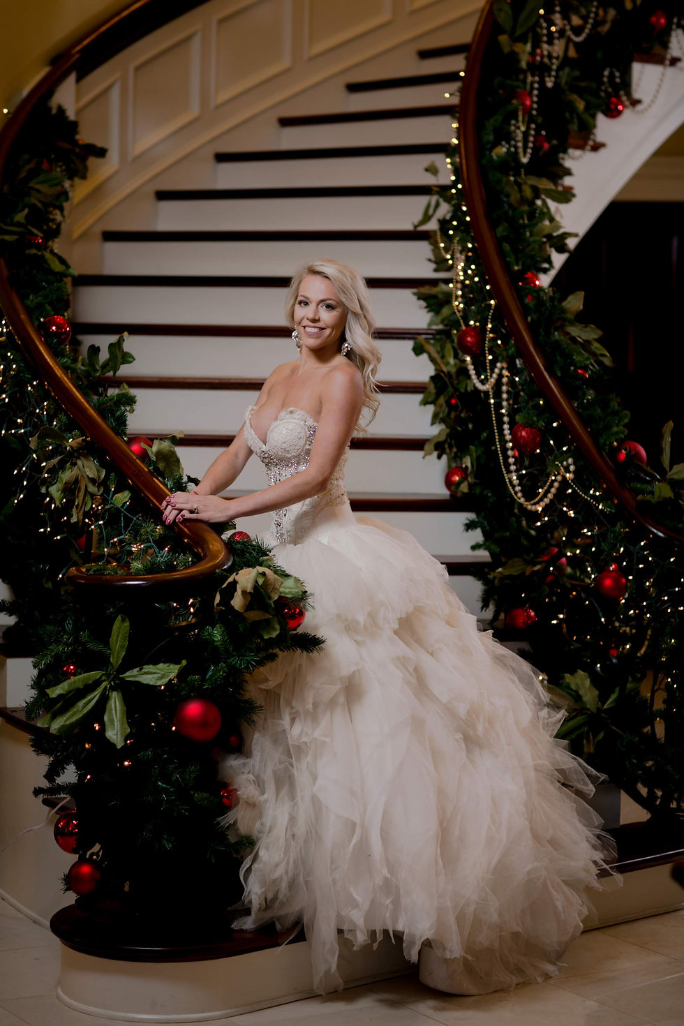 Bride posing on a grand staircase decorated with Christmas greenery, red ornaments, and warm string lights