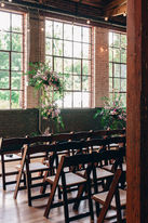 A moody indoor wedding venue with wooden chairs and large windows allowing natural light to filter in.