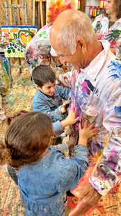 הנכדים מחבקים את סבא שלהם עם כפות ידיים מלוכלכות בצבע, כולם צוחקים