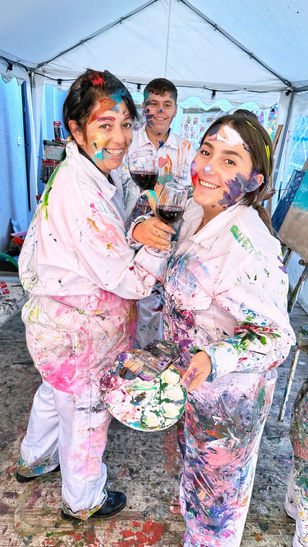 שלושה מבני המשפחה, שתי בנות ובן, מסתכלים על המצלמה ומחייכים, כשהפנים וסרבל הציור שלהם מצוירים וצבעוניים