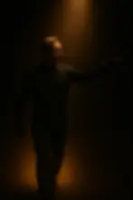 David walks through a dark alien corridor, illuminated by a narrow beam of warm light.