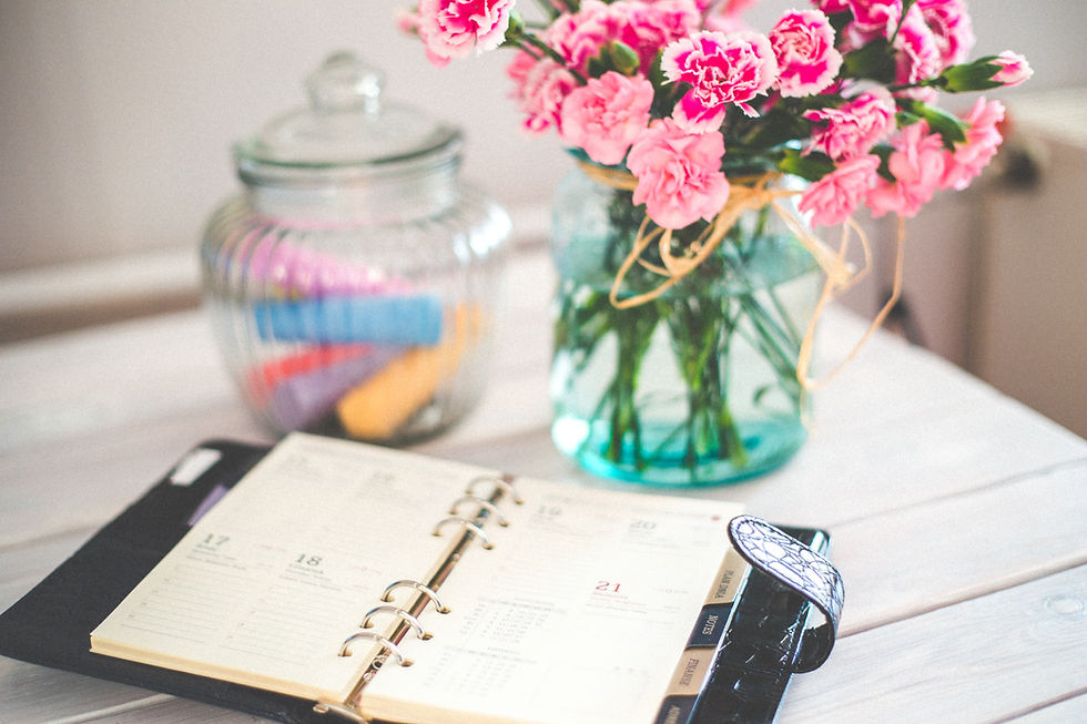 Planner on a table. Pink flowers in a clear vase and a glass jar with colorful chalk.