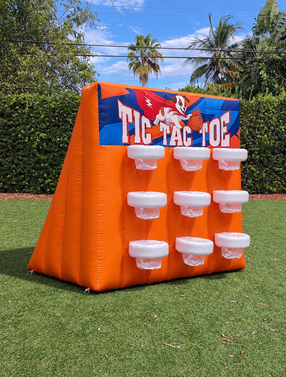 Orange-and-blue Tic Tac Toe Basketball inflatable on grass, featuring a three-by-three arrangement of white basket targets and a colorful sign at the top.