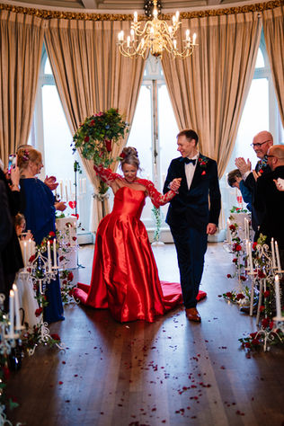 bride in bright red dress cheering with arm in air after being married 
