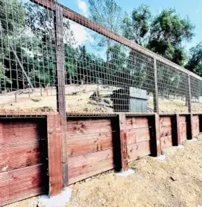 Wooden fence stands tall with wire mesh, trees in the background.