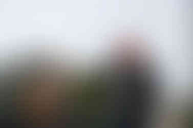 A guitar player with facial hair and a fedora plays next to a man in a red cap and leather jacket who sings.