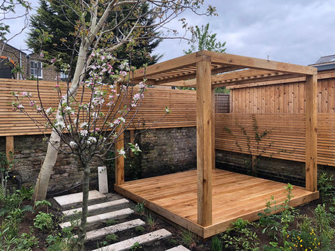 An oak pergola with oak decking set against larch horizontal batten fencing with an apple tree in the foreground