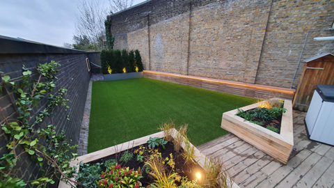 A london garden with oak sleepers beds and cedar bench. Big house wall on the right and boundary wall on the left