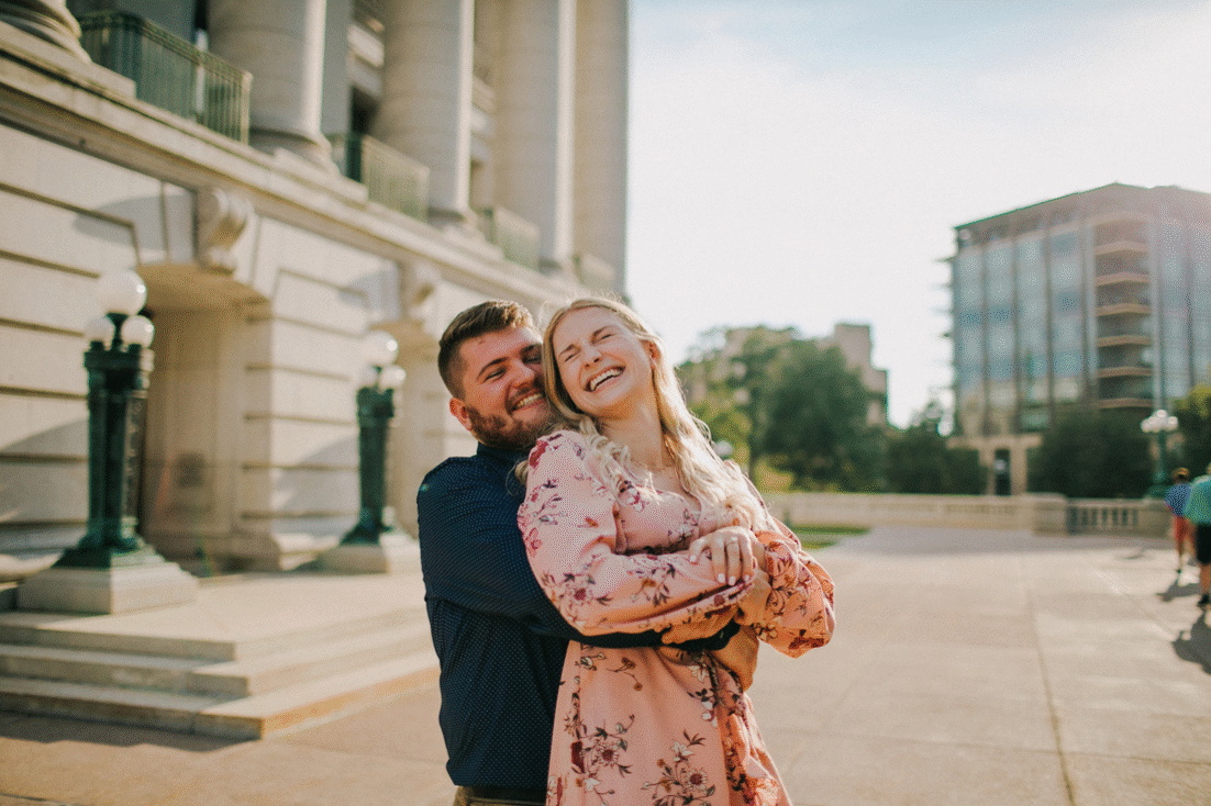 A man hugs a woman from behind in front of the Wisconsin State Capitol