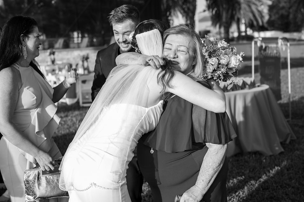 Bride and the groom's grandmother hugging after the wedding while the groom is wiping a tear away while speaking with a family memeber.