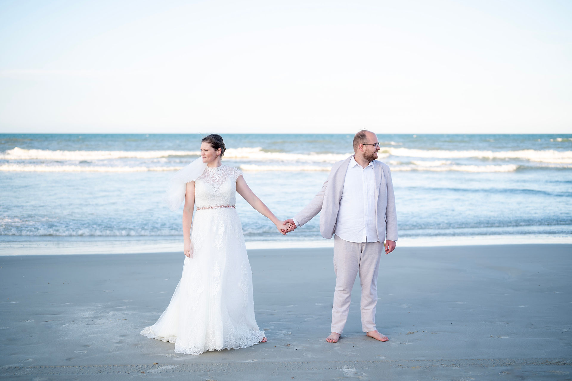 Bride and groom holding hands looking at the opposite direction with the ocean in the background