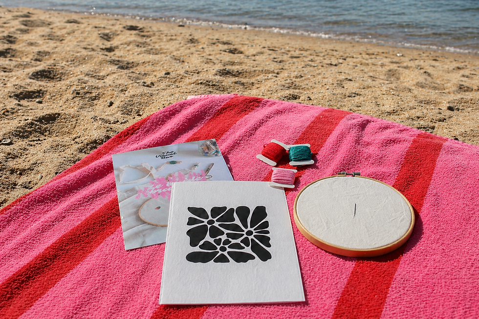 Une serviette de plage posée sur le sable, avec un kit de broderie posé sur la serviette
