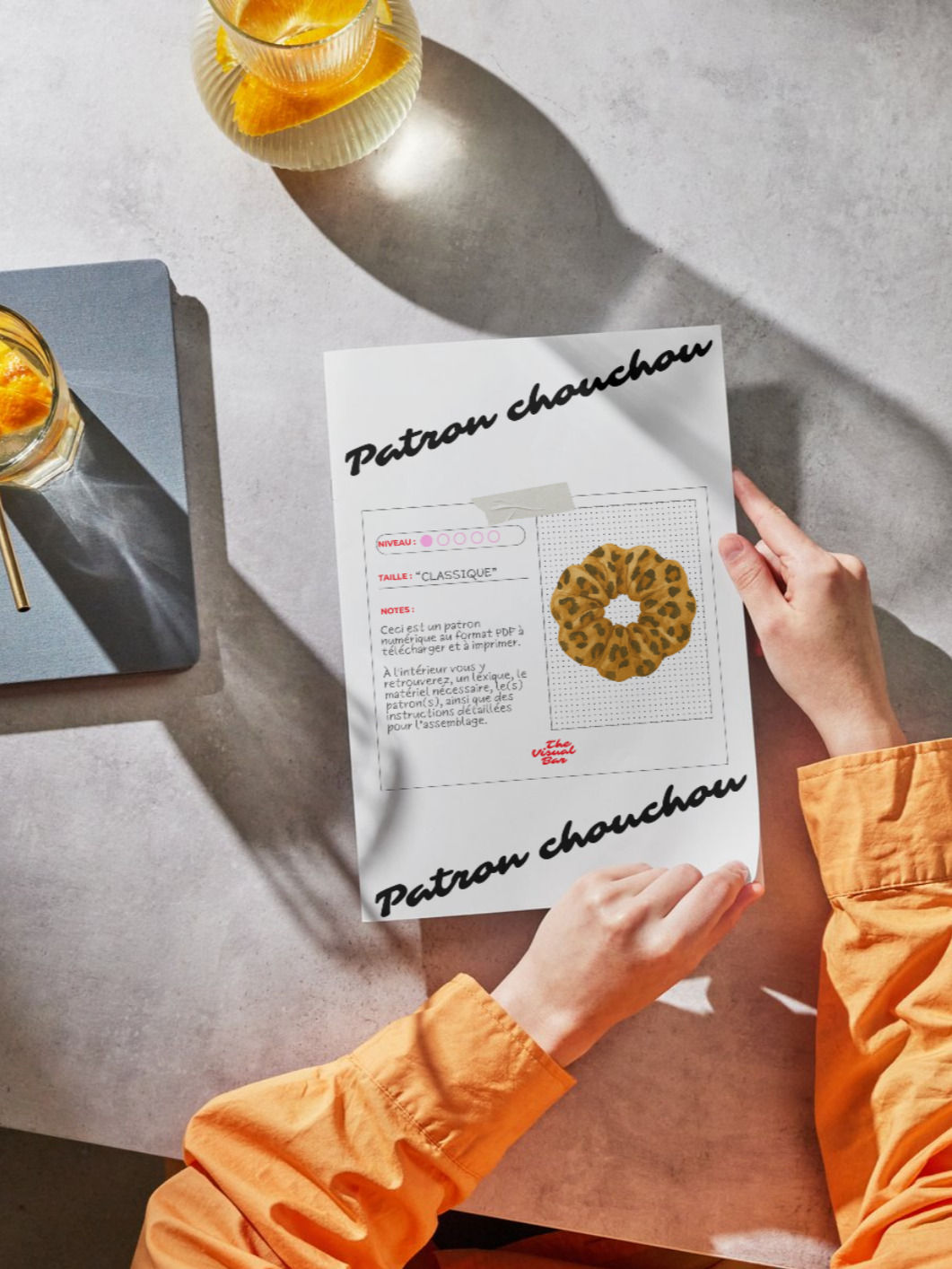Personne tenant un patron de chouchou en PDF imprimé, posé sur une table,dans une ambiance lumineuse et minimaliste.