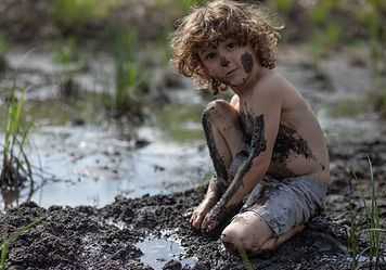 A young boy is covered in mud and dirt in a swamp at the park. The kid is at camp, playing